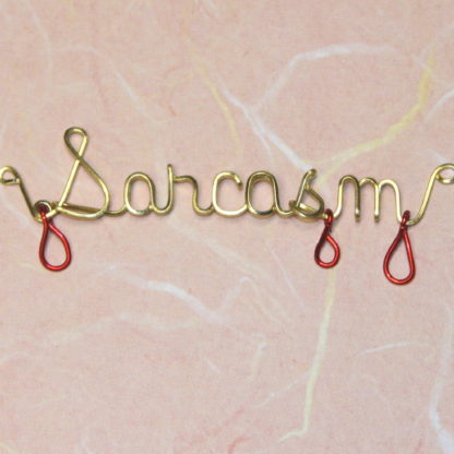 Sarcasm wirtten in brass wire with red drips